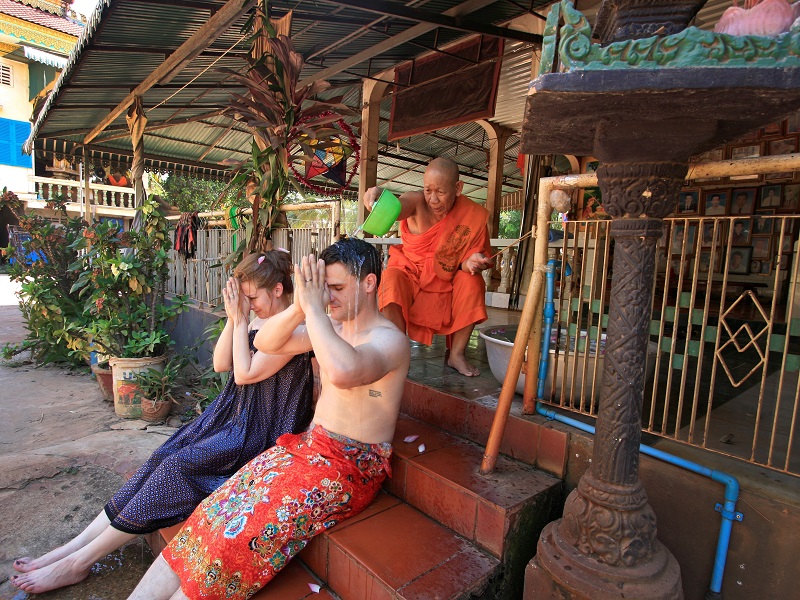 Newlywed couple being water blessed by monk