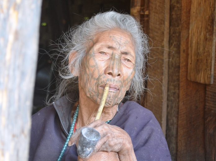 Elder Burmese woman with face tattoos smoking from a pipe
